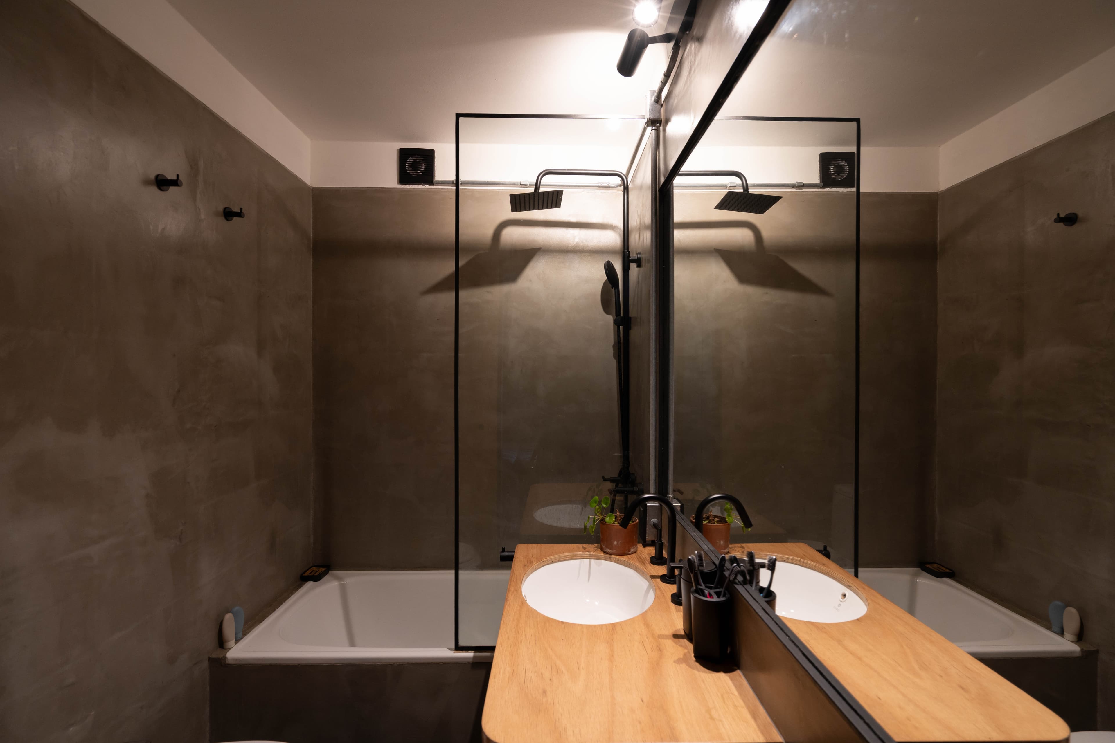 Baño con ducha tipo lluvia, bañera y doble bacha sobre mesada de madera
