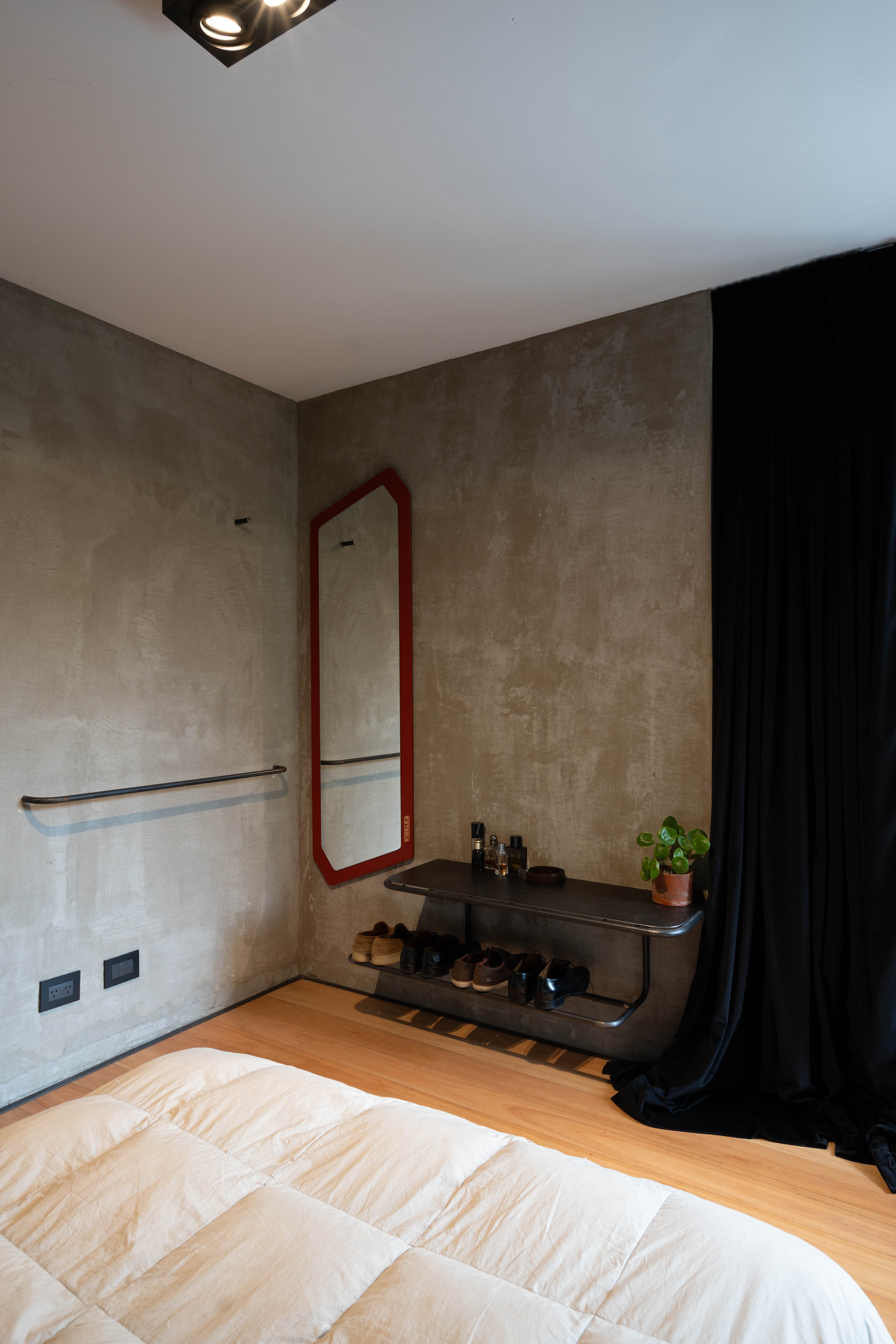 Rincón de habitación con espejo rojo, mueble bajo y planta