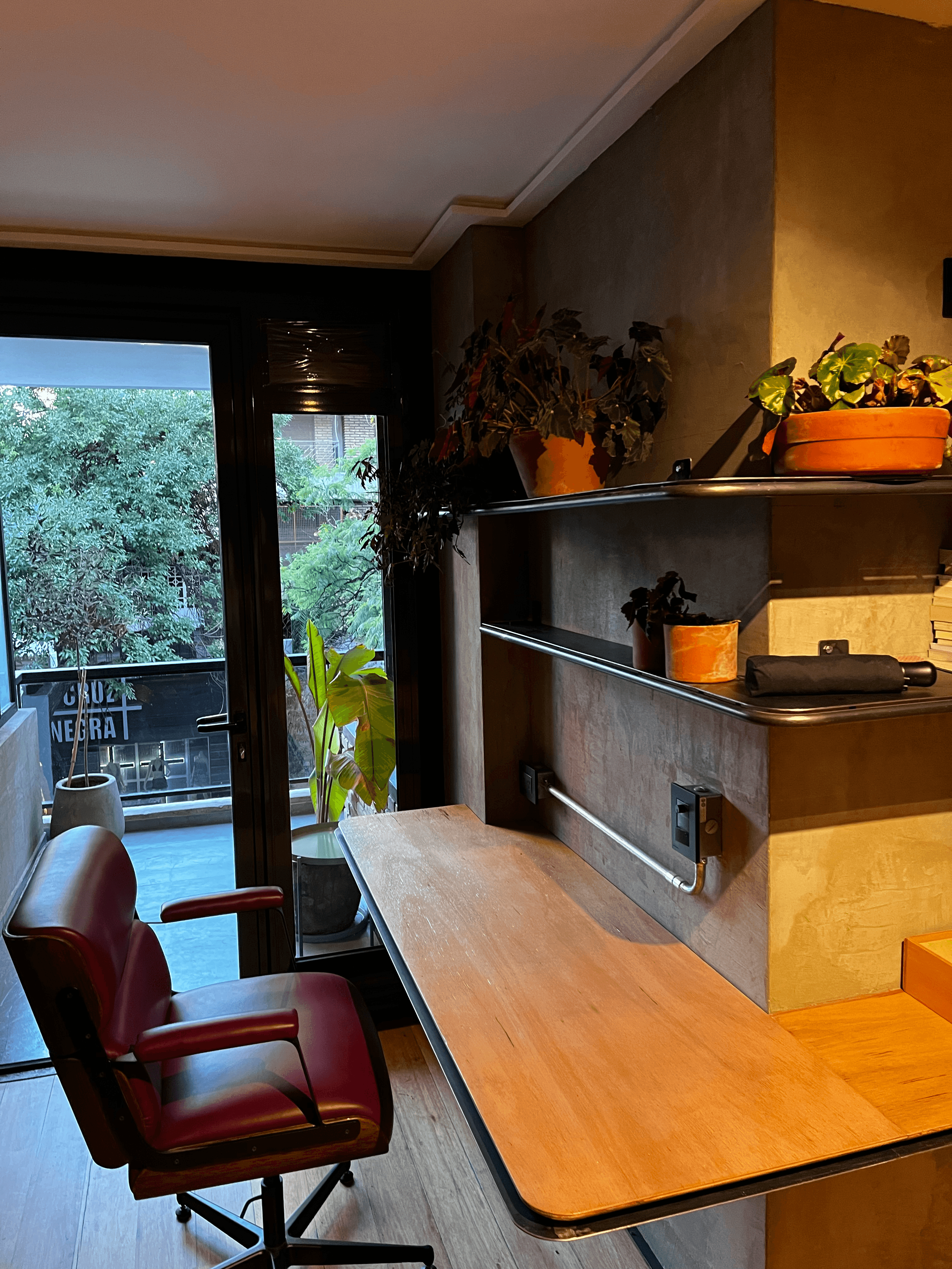Zona de trabajo con mesa sin patas, silla de cuero roja, plantas y balcón